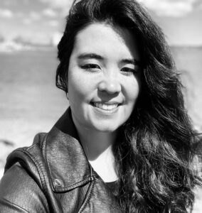 A smiling woman with long hair wearing a leather jacket outdoors.