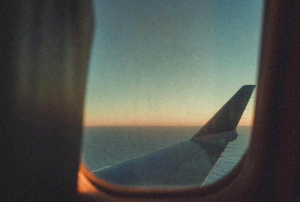 View of a sunset through an airplane wing window, flying over the sea.