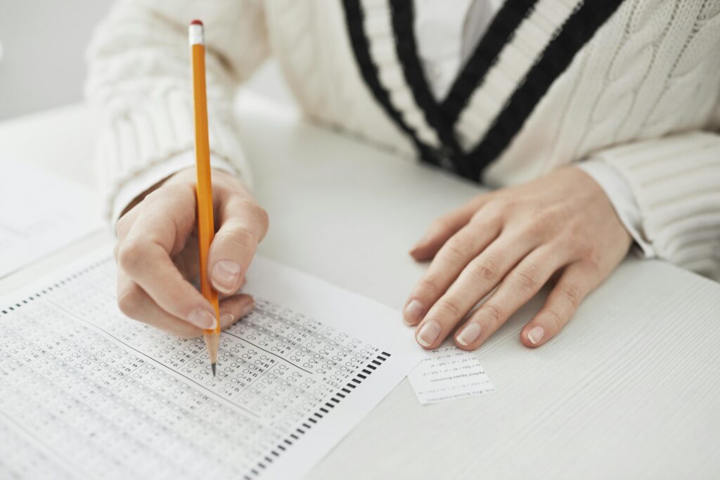 A student writing answers on a multiple-choice exam sheet at a desk.