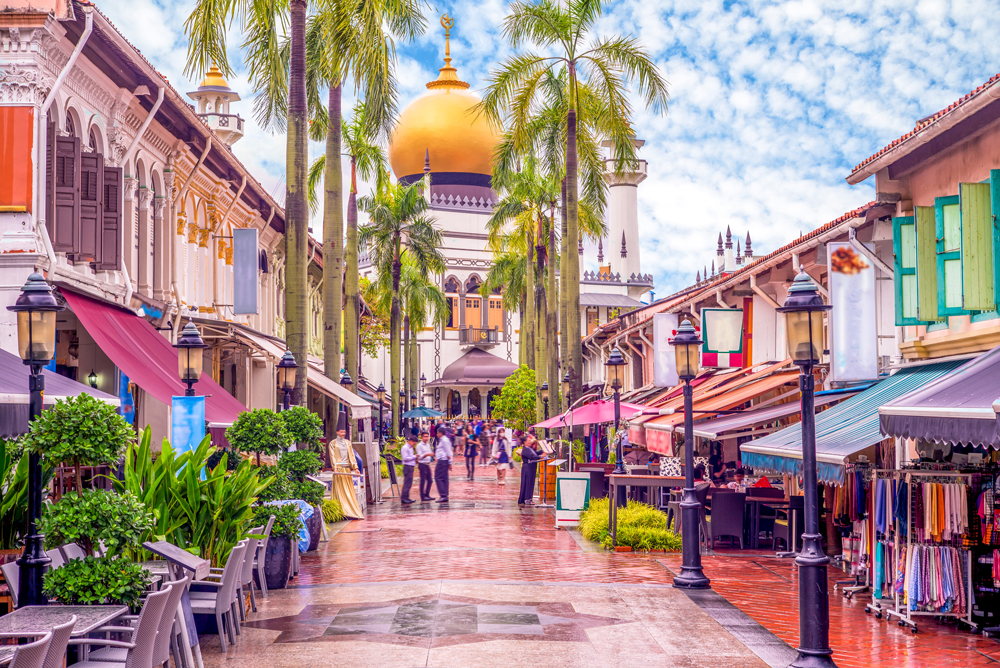 A vibrant street with palm trees and a golden-domed mosque in the background.