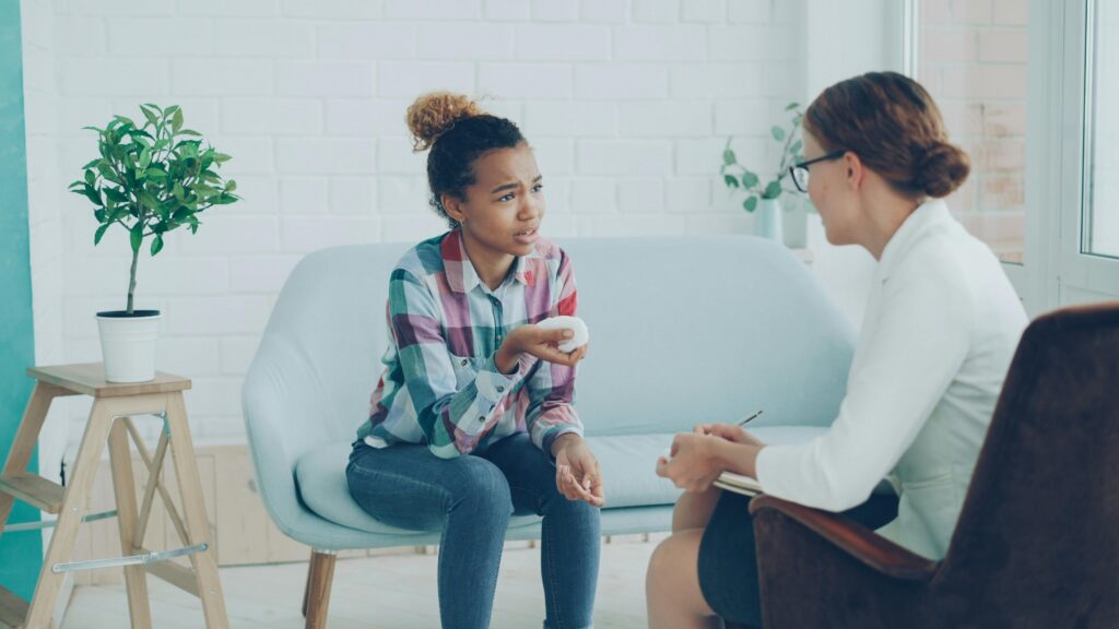 A young woman in discussion with a counselor during a session. Modern, bright office setting.